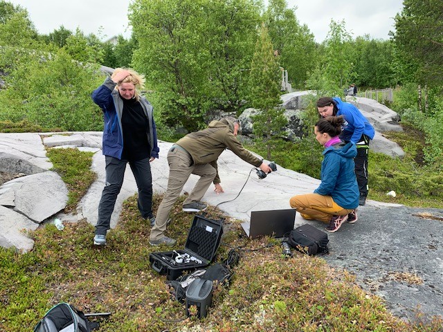 Fotot visar tre personer vid en häll, en av personerna 3D-skannar hällristningar med handhållen laserskanner.