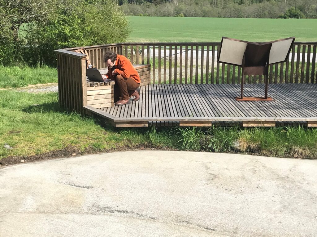 Fotot visar en person på huk framför en laptop, i förgrunden syns en berghäll.