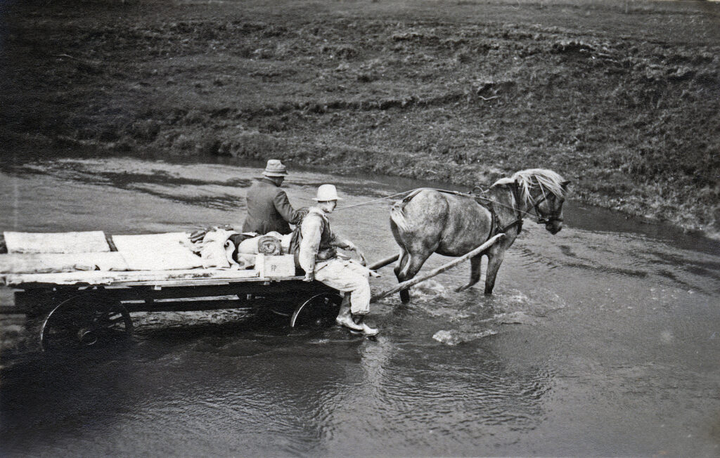 Svartvitt foto på en häst som drar en kärra, på kärran sitter två personer, bakom dem ligger gipsavgjutningar.