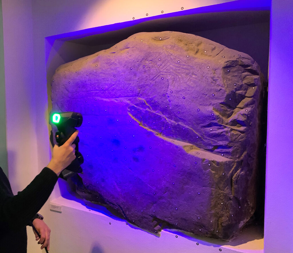 Fotot visar ett stenblock med hällristningar som skannas med handhållen 3D-skanner.